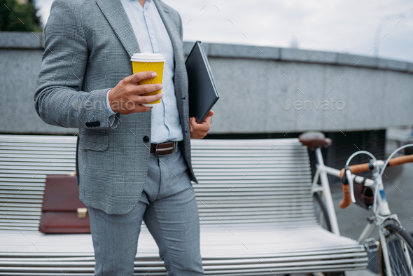 Businessman with cycle drinks coffee on the bench - Stock Photo - Images