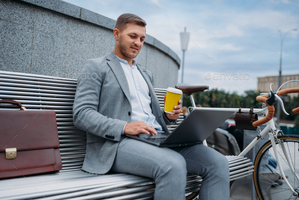 Businessman with bike drinks coffee on the bench
