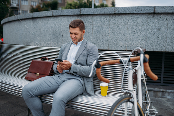 Businessman with bike talking by phone on bench
