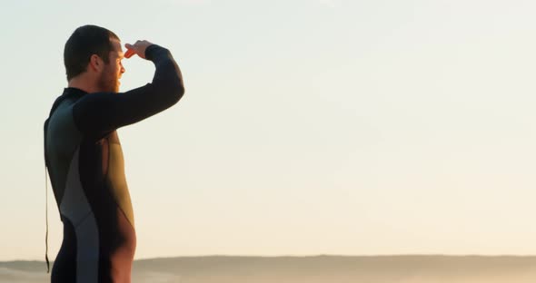Side view of mid-adult caucasian male surfer with shielding eyes looking at sea at beach 4k alt