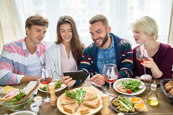 Friends Watching Video at Dinner Table - Stock Photo - Images