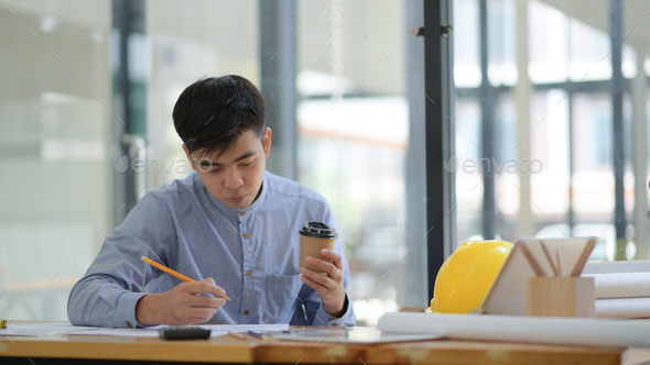 Engineering is checking floor plan in office.He held a pencil and coffee cup in hand and seriously. - Stock Photo - Images