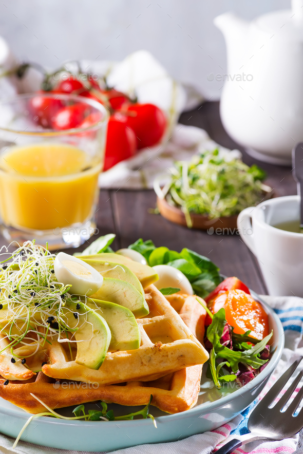 Belgian Waffles with avocado, eggs, micro green and tomatoes with orange juice on wooden table - Stock Photo - Images