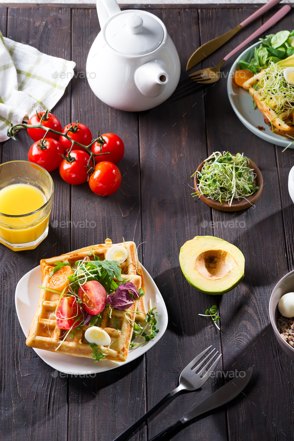 Belgian Waffles with avocado, eggs, micro green and tomatoes with orange juice and tea on wooden - Stock Photo - Images