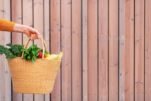 Girl holding basket with healthy organic vegetables, wooden background, copy space. Autumn harvest - Stock Photo - Images