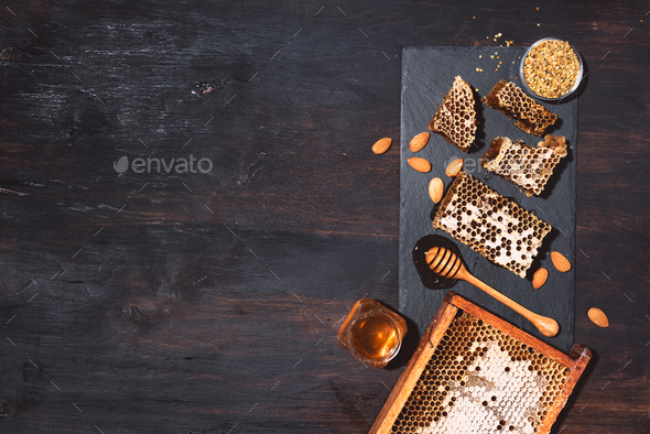 Honeycomb, bee pollen granules, honey jar with wooden dipper, almond nuts on black slate tray over - Stock Photo - Images