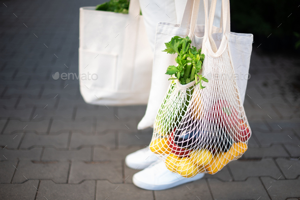 Girl holding mesh shopping bag and cotton shopper with vegetables without plastic bags at farmers - Stock Photo - Images