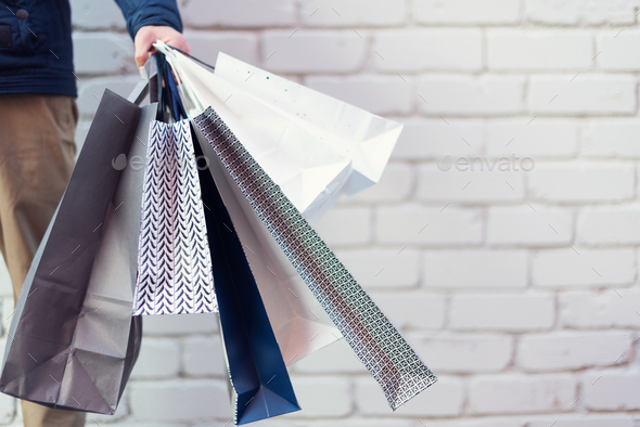 Male hand holding bunch of shopping bags with purchases near brick background. Copy space. Sale - Stock Photo - Images