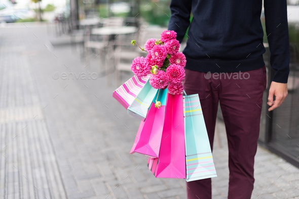Stylish man holding flowers and pink, blue shopping bags near restaurant. Woman's day. Valentine - Stock Photo - Images