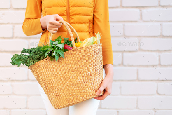 Young girl holding straw basket with vegetables, products without plastic bags, brick background - Stock Photo - Images