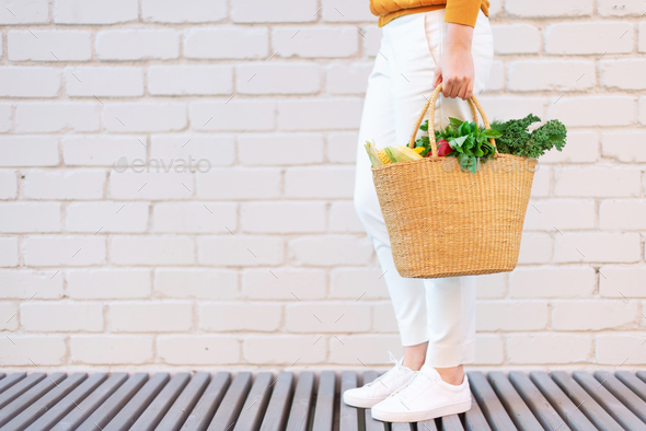 Young girl holding straw basket with vegetables, products without plastic bags, brick background - Stock Photo - Images