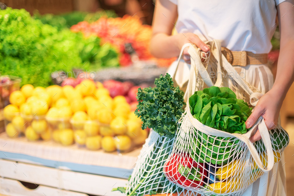 Girl holding mesh shopping bag and cotton shopper with vegetables without plastic bags, wooden - Stock Photo - Images