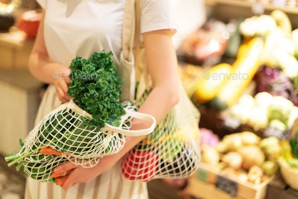 Girl holding mesh shopping bag and cotton shopper with vegetables without plastic bags, wooden - Stock Photo - Images