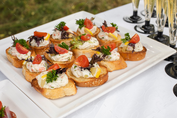 Delicious canape with sausage and tomato.Canapes on white ceramic plates at wedding reception - Stock Photo - Images