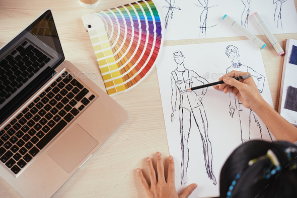 Crop fashion designer sketching near laptop