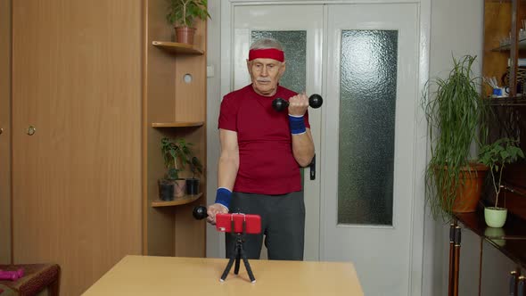 Senior Elderly Mature Man Watching Online Distance Workout Exercises with Dumbbells on Mobile Phone alt