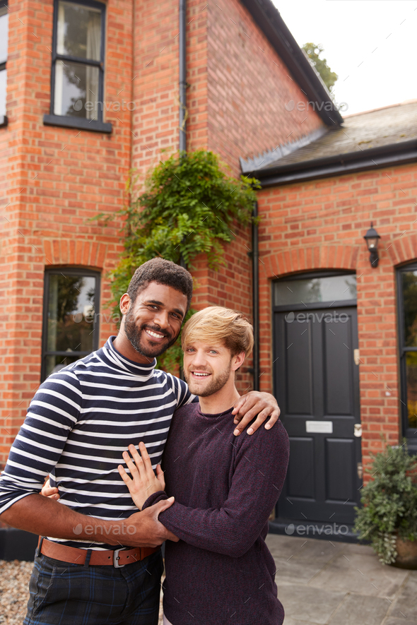 Portrait Of Excited Gay Male Couple Standing Outside New Home On Moving Day Together