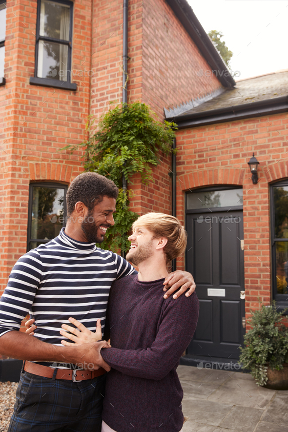 Excited Gay Male Couple Standing Outside New Home On Moving Day Together