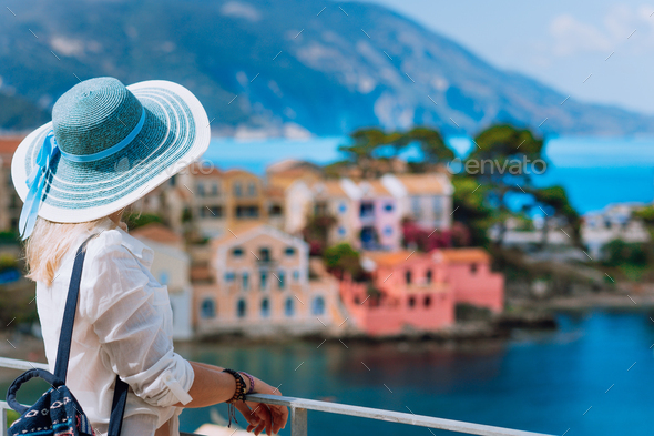 Tourist woman in blue sunhat and white clothes enjoying top view of colorful tranquil village Assos