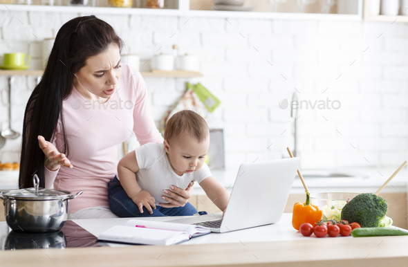 Shocked mother looking at her baby clicking on laptop - Stock Photo - Images