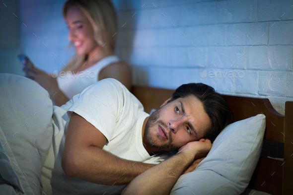 Girlfriend Texting On Phone Lying With Boyfriend In Bed, Low-Light - Stock Photo - Images