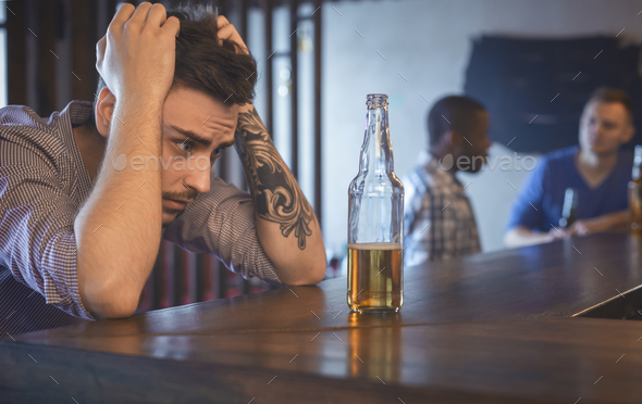 Troubled young man sitting alone at bar