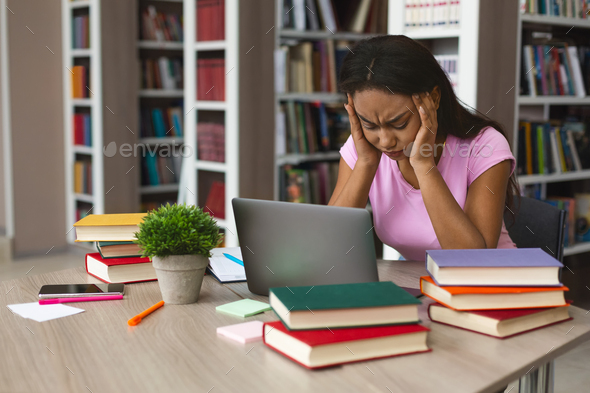 Tired afro girl stucked with laptop and books at library - Stock Photo - Images