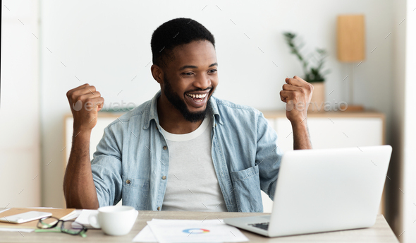 Black employee looking at laptop screen and celebrating success