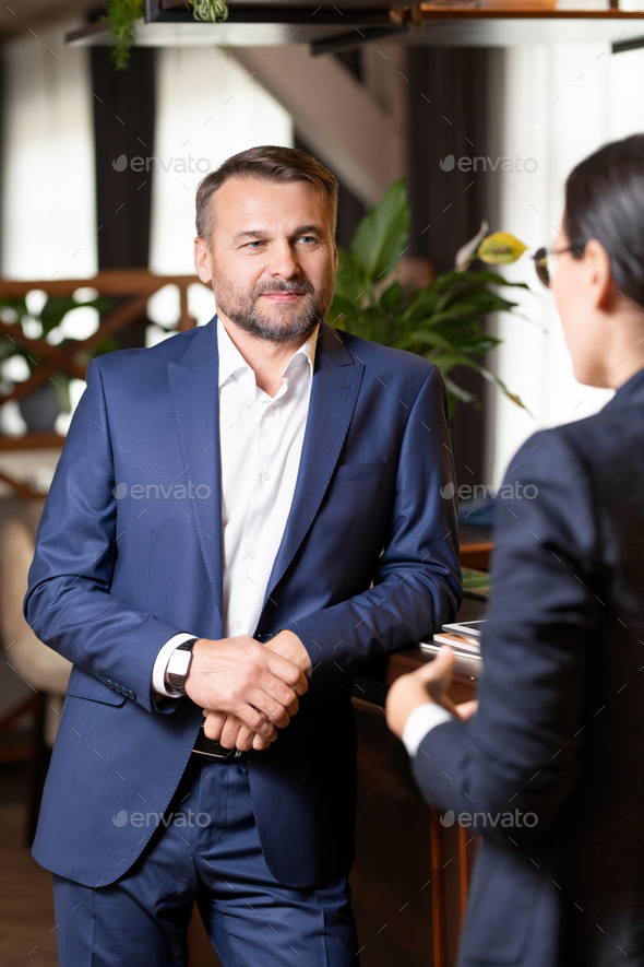 Mid-aged businessman standing by bar counter during interaction with colleague