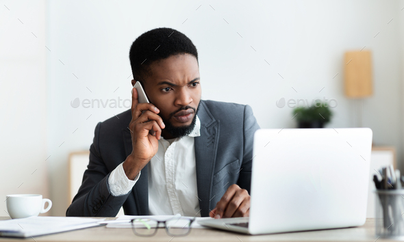 Concerned businessman talking on cellphone and looking at laptop screen