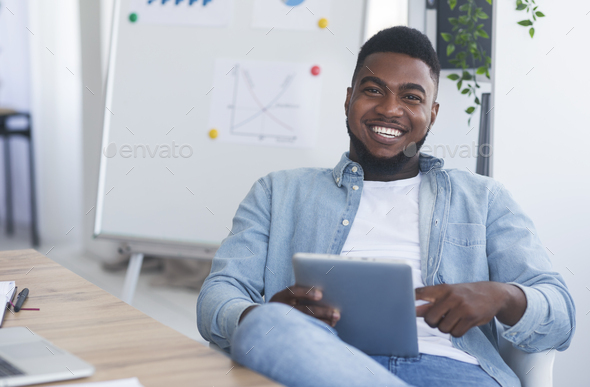 Cheerful business coach holding digital tab, sitting in modern office