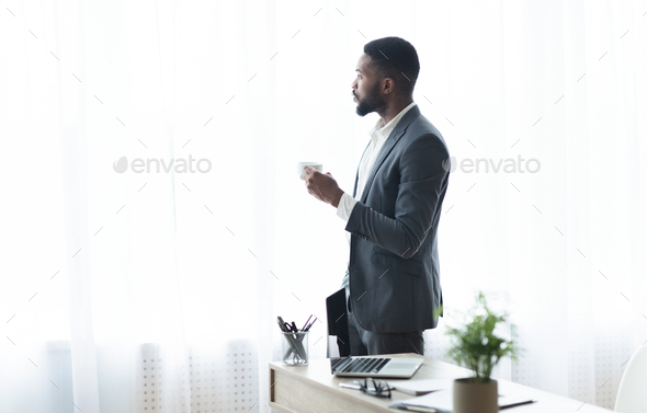 Thoughtful black businessman looking out of window and drinking coffee