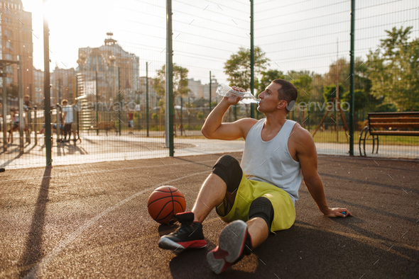 Basketball player drinks water on outdoor court - Stock Photo - Images