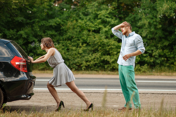 Man and woman pushing broken car on road - Stock Photo - Images
