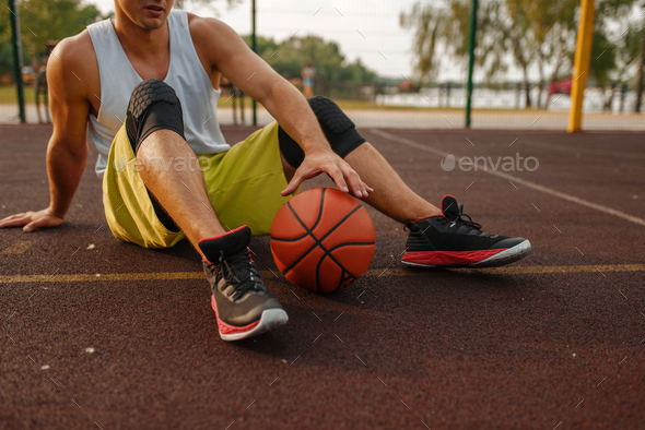 Basketball player with ball sitting on the ground - Stock Photo - Images