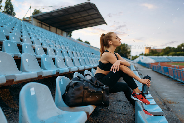 Female runner sitting on tribune and drinks water - Stock Photo - Images