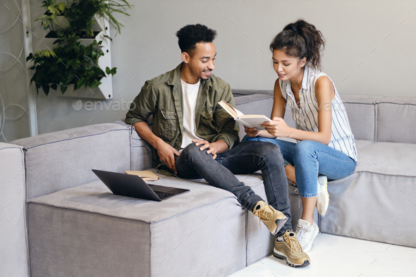 African American man and pretty Asian woman happily reading book together in modern co-working