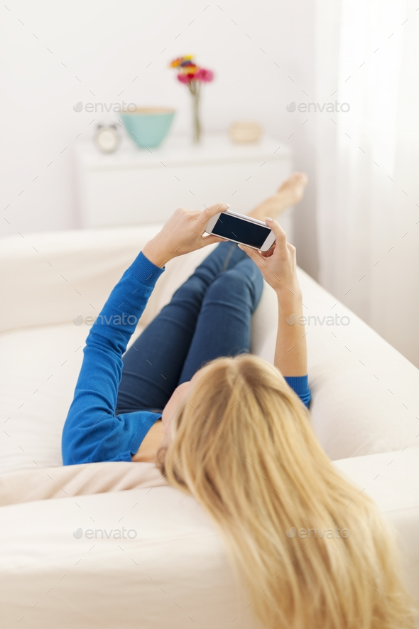 Blonde woman lying down with smart phone on sofa