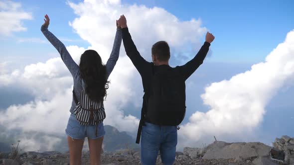 Young Couple of Tourists with Backpacks Reaching Up Top of Mountain and Raised Hands. Man and Woman alt