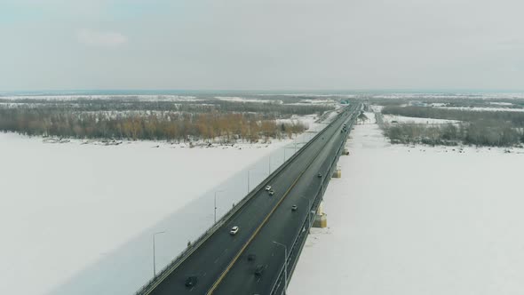 Cars Drive Along Gray Bridge Making Shadow on Frozen River alt