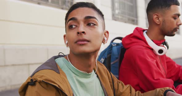 Two mixed race male friends wearing headphones, listening to music in the street alt