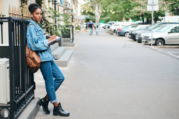 African American student girl in denim jacket with backpack confidently looking in camera on street - Stock Photo - Images