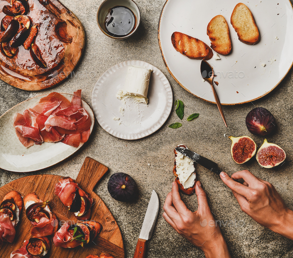 Crostini with prosciutto, figs and female hands spreading goat cheese - Stock Photo - Images