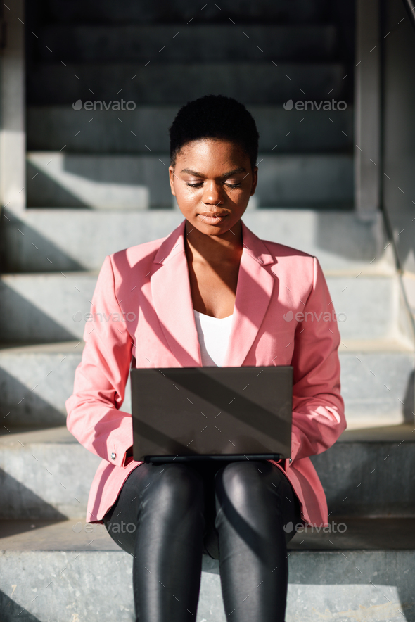 Black woman sitting on urban steps working with a laptop computer - Stock Photo - Images