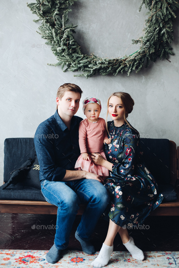 parents and daughter sitting on sofa under big fir wreath - Stock Photo - Images