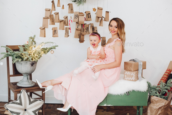 Beautiful mom with little daughter in pink dresses playing near Christmas decoration - Stock Photo - Images
