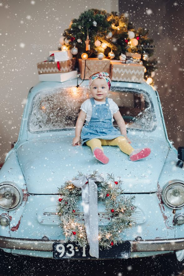 Front view of sweet and fashionable little cute girl sitting on blue retro car decorated for - Stock Photo - Images