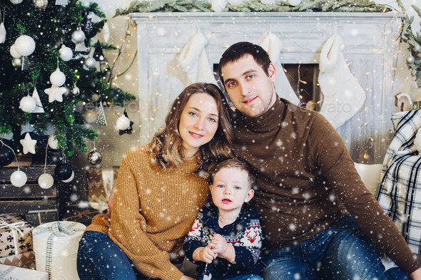 Family sitting together on sofa in decorated studio near Christmas tree - Stock Photo - Images