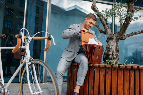 Businessman bicyclist puts document into briefcase - Stock Photo - Images