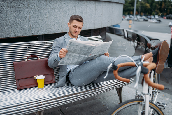 Businessman with bike reading newspaper on bench